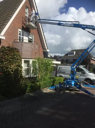 Schilder in de bak van een blauwe hoogwerker bij een dakkapel.