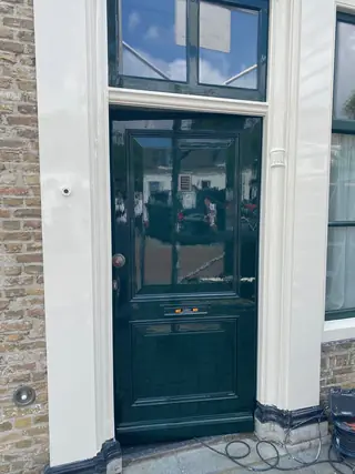 Donkergroene voordeur met wit kozijn in een gemetselde gevel.