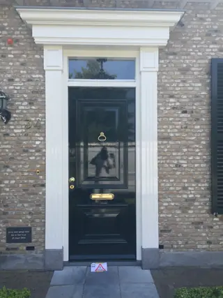 Zwarte voordeur met een wit omlijst kozijn in de gevel van een monumentaal pand.