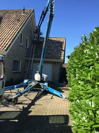 Blauwe rupshoogwerker uitgestempeld op een oprit, met de arm langs de dakrand.