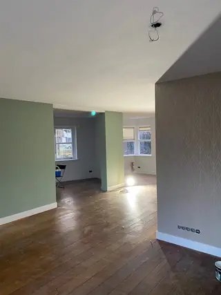 Lege woonkamer met houten vloer en zachtgroene wanden, met doorkijk naar de volgende kamer.