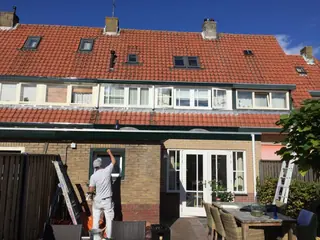 Schilder op een ladder bij de kozijnen van een rij woningen met rode pannendaken.