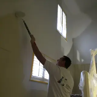 Schilder rolt met een verlengde roller een hoog plafond wit.