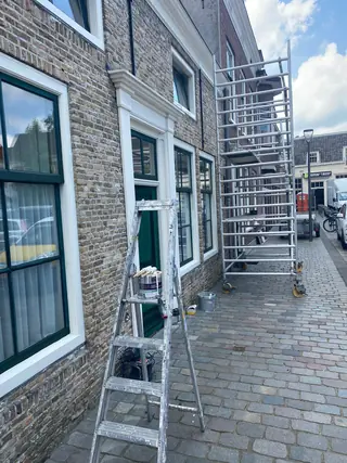Rolsteiger en trapladder tegen een gemetselde gevel met pas geschilderde witte kozijnen.