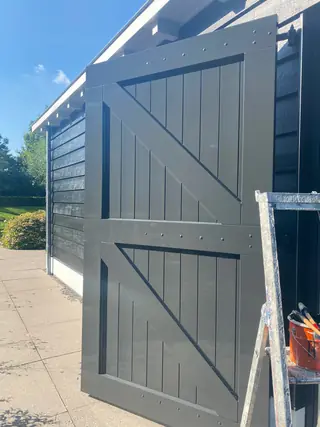 Grijsgroen geschilderde houten schuurdeuren met een ladder ernaast.
