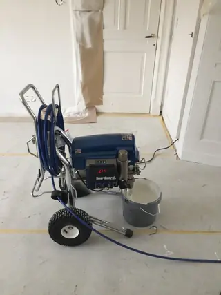 Spuitpomp met slang in een leeggehaalde kamer, met de deuren afgeplakt.
