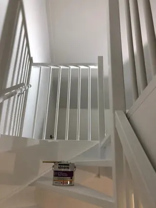 Wit geschilderde trap met balusters en een geopend verfblik op een tree.