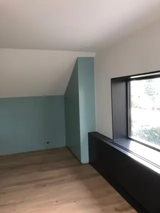 Zolderkamer met een mintgroene wand naast een breed venster.