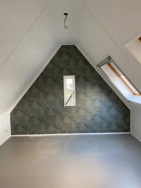 Zolderkamer met witte wanden en een topgevel behangen met een donkergroen bladpatroon.