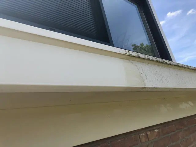 Witte dakgoot en boeiboord langs een dakrand, deels aangeslagen, met een dakraam erboven.
