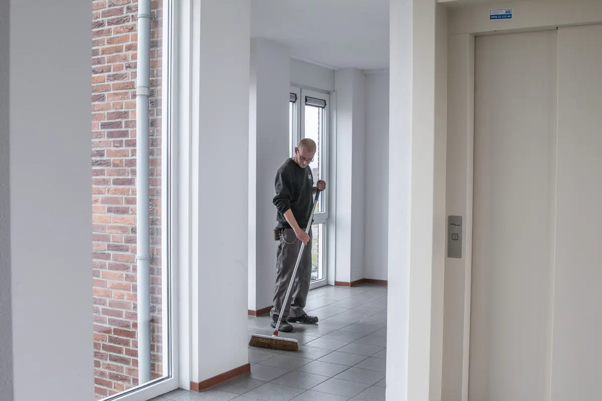 Medewerker van Delta veegt de tegelvloer van een entree met lift en bakstenen binnenwand.