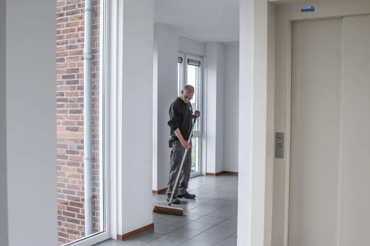 Medewerker van Delta veegt de tegelvloer van een entree met lift en bakstenen binnenwand.