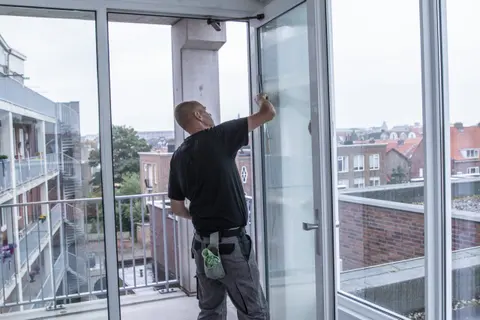 Medewerker van Delta zeemt de binnenkant van een galerijraam, met de daken van Vlissingen erachter.