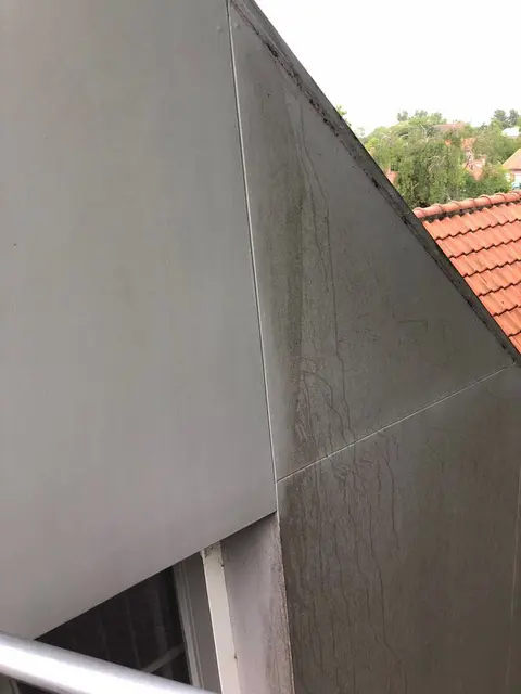 Gevelplaat waarop de grens tussen het gereinigde en het nog niet gereinigde deel te zien is.