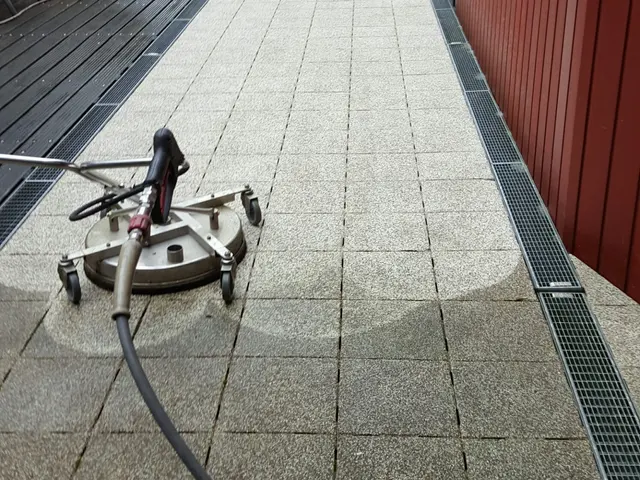 Roterende schrobschijf met slang op een bestrating tussen twee gebouwen, met een schoongemaakte baan eromheen.