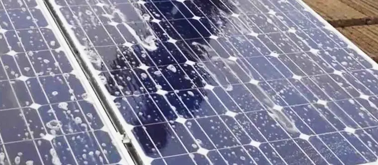 Zonnepanelen op een dak, nat van het water, met de weerspiegeling van een persoon erin.