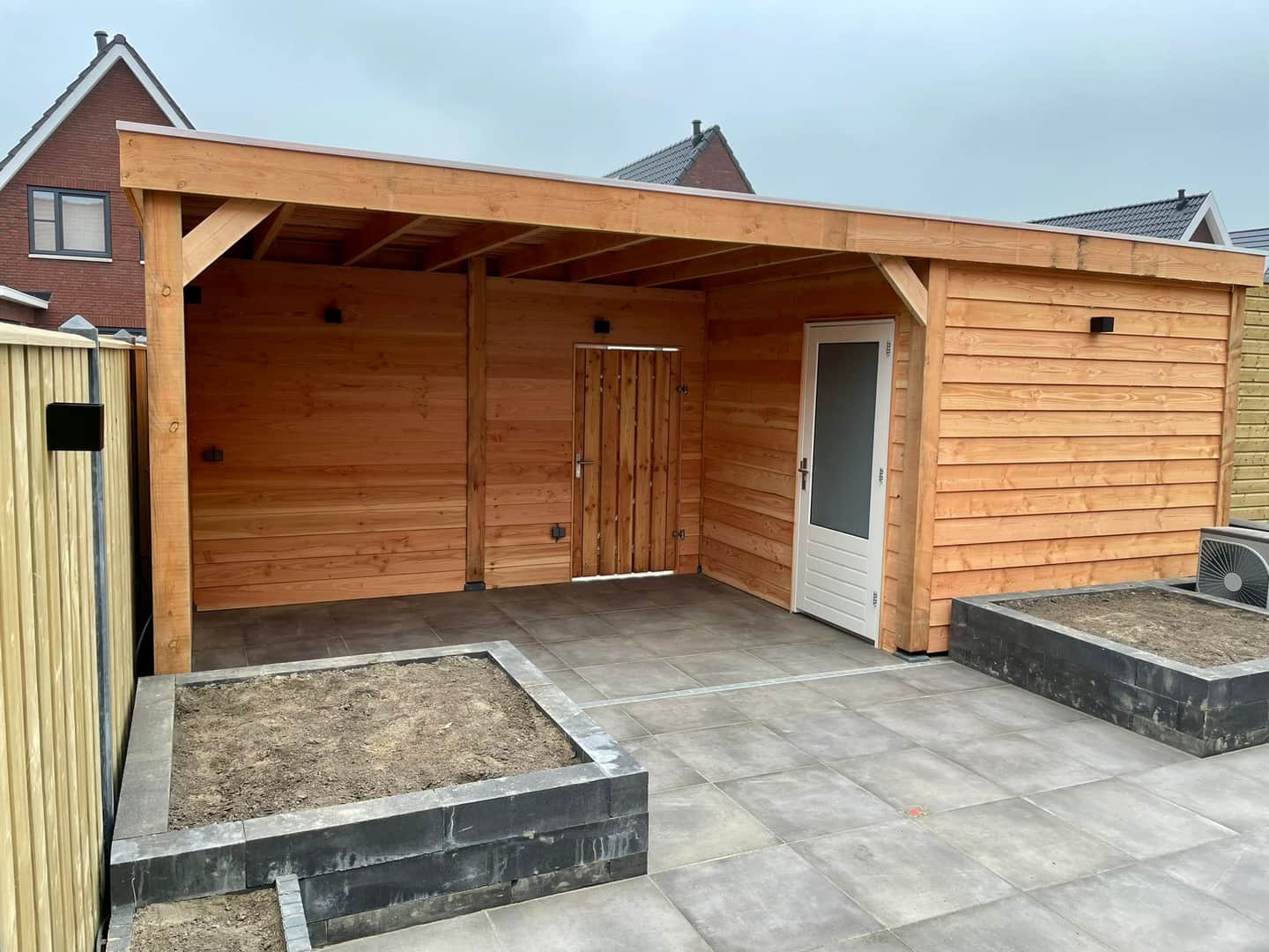 Nieuwe houten overkapping met berging en aangrenzende plantvakken in aanbouw