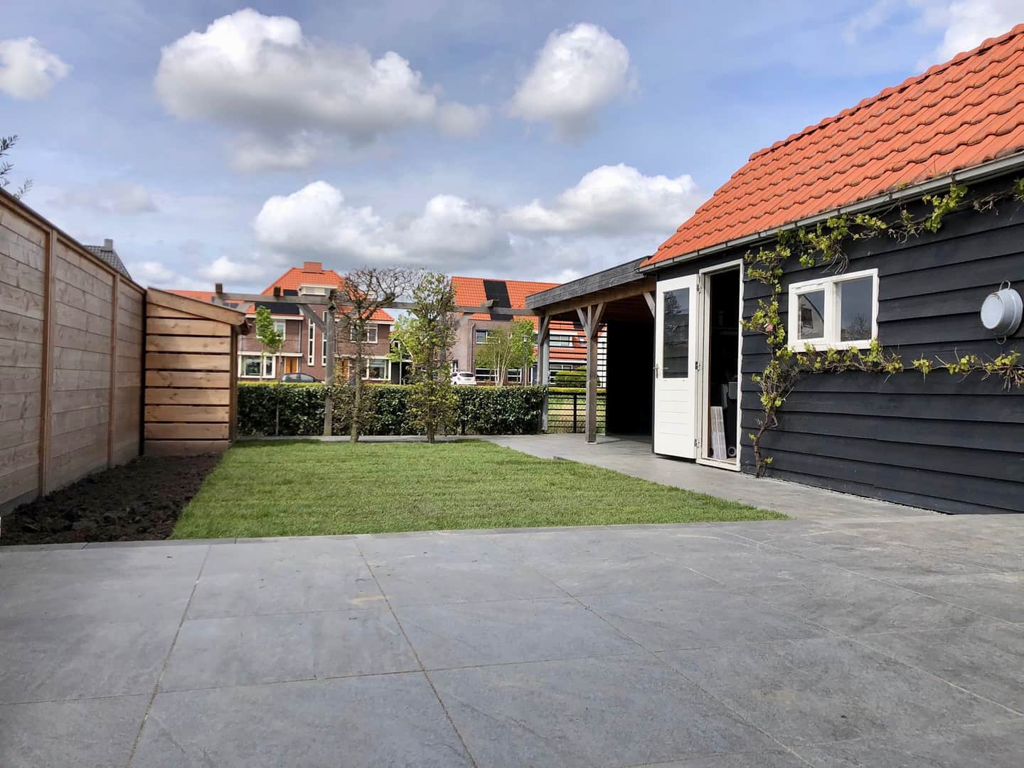 Achtertuin met nieuw gazon en een ruim terras naast een zwart houten schuur