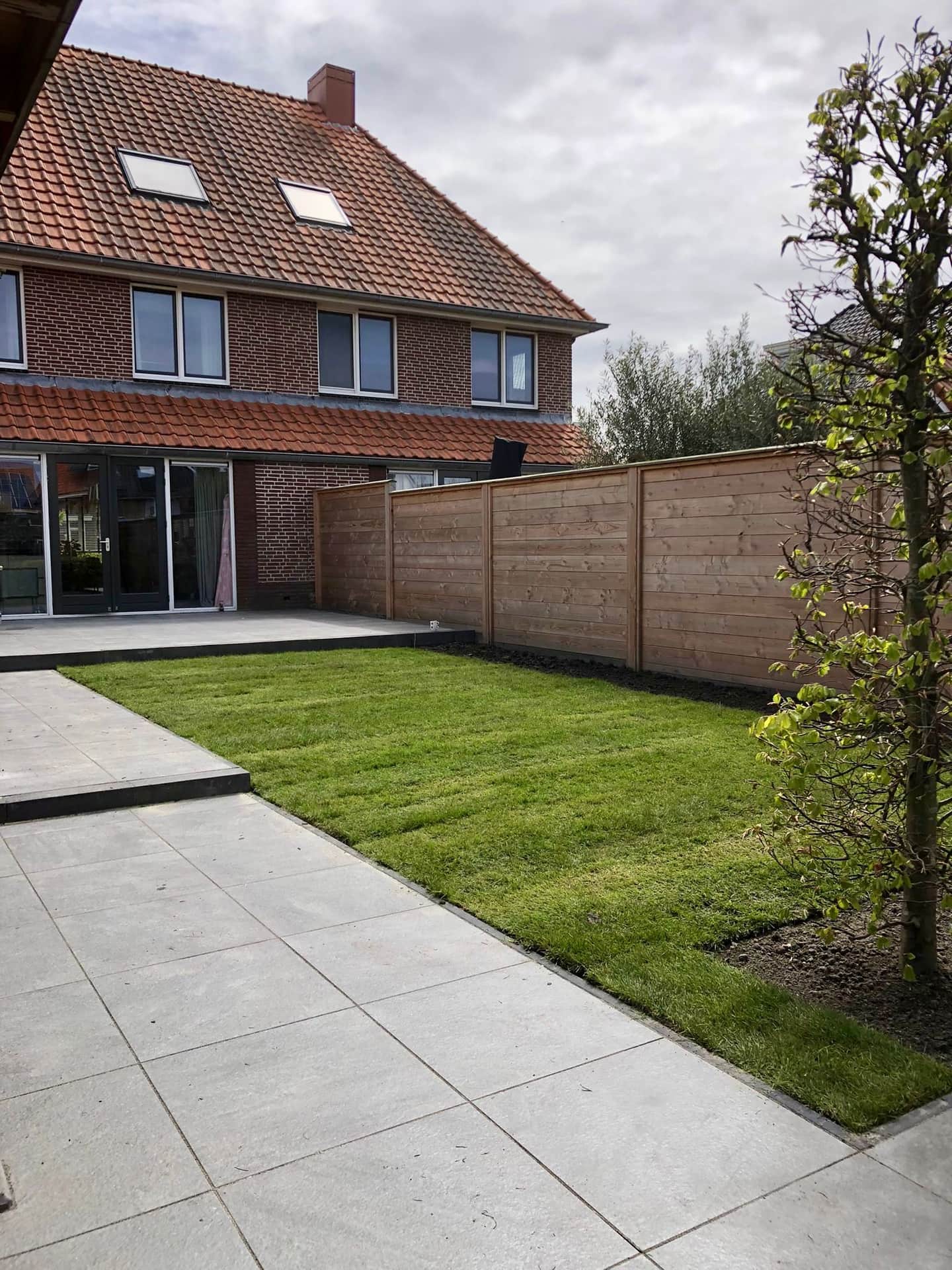 Vers gelegde graszoden naast een nieuw terras van grote grijze tegels