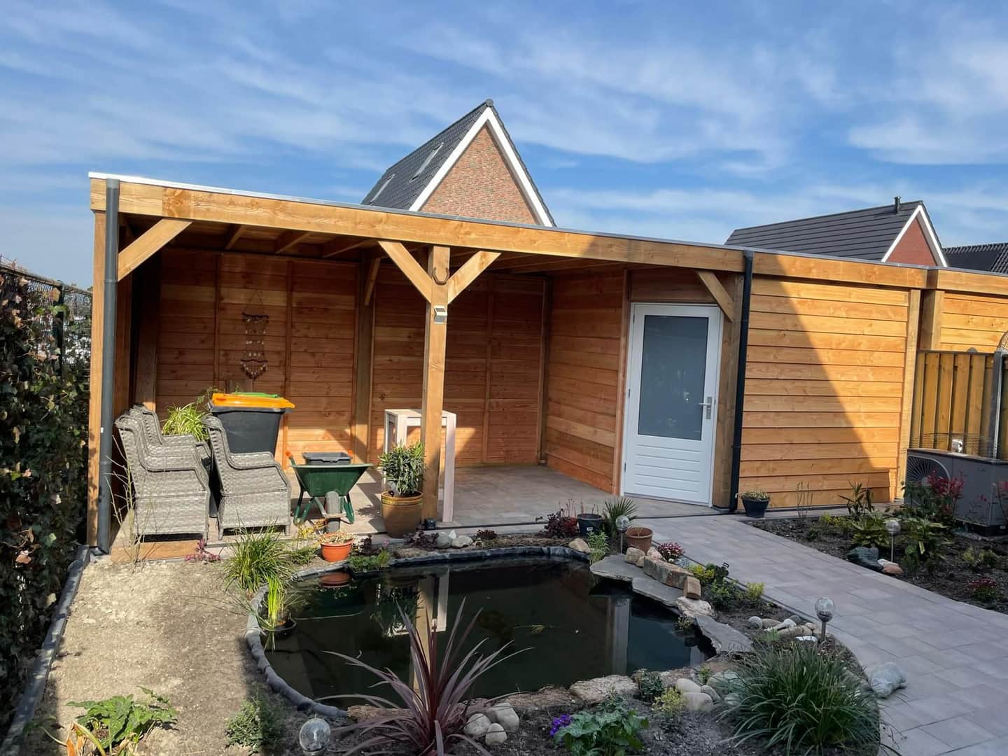 Houten overkapping met zitplek en een vijver met beplanting ervoor