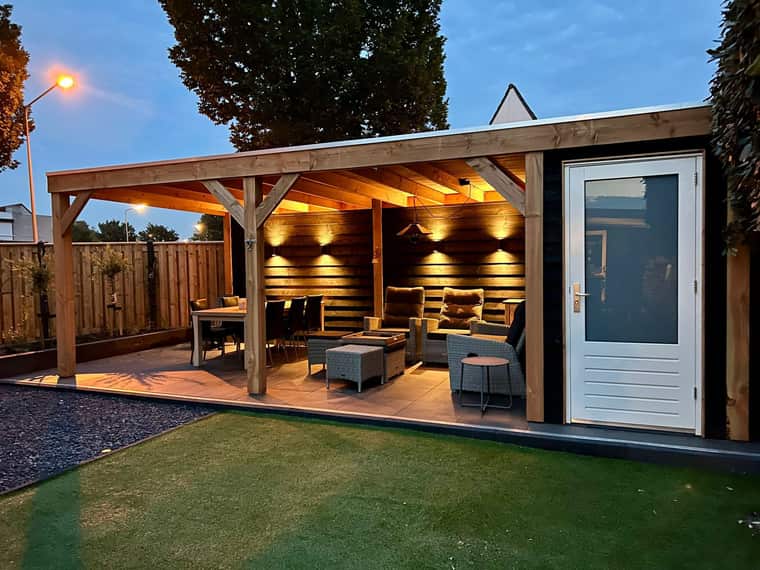 Houten overkapping met loungeset en warme spots, gefotografeerd in de schemering