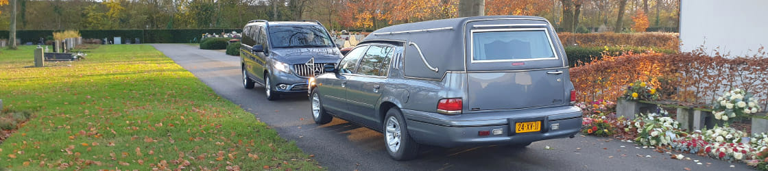 Rouwauto en volgauto op een begraafplaats in de herfst