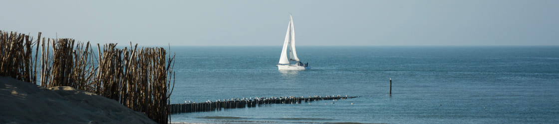 Een zeilboot voor de kust achter een rij paalhoofden