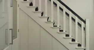 Kast onder een trap met witte panelen en een lange greep.