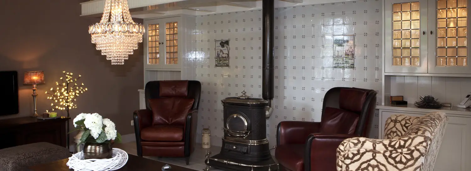 Klassieke woonkamer met ingebouwde kasten met glasdeurtjes langs een betegelde wand en een kachel.