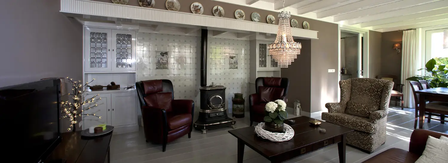 Klassieke woonkamer met een ingebouwde kast met glasdeurtjes, een kachel en twee leren fauteuils.