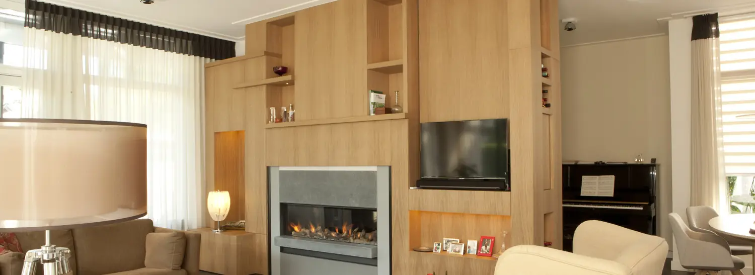 Woonkamer met een wandmeubel in eiken rond een brandende haard, met open vakken en warme verlichting.