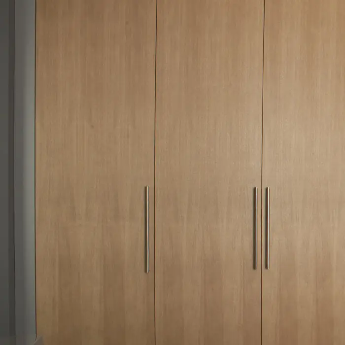 Kastenwand in licht eiken met hoge deuren en slanke grepen in een slaapkamer.