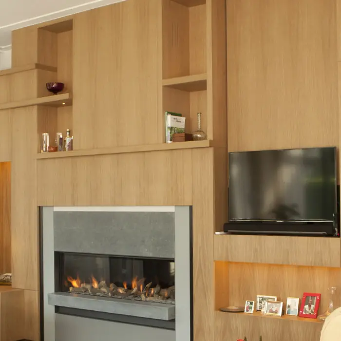 Wandmeubel in eiken met open vakken rond een ingebouwde haard en een televisie.
