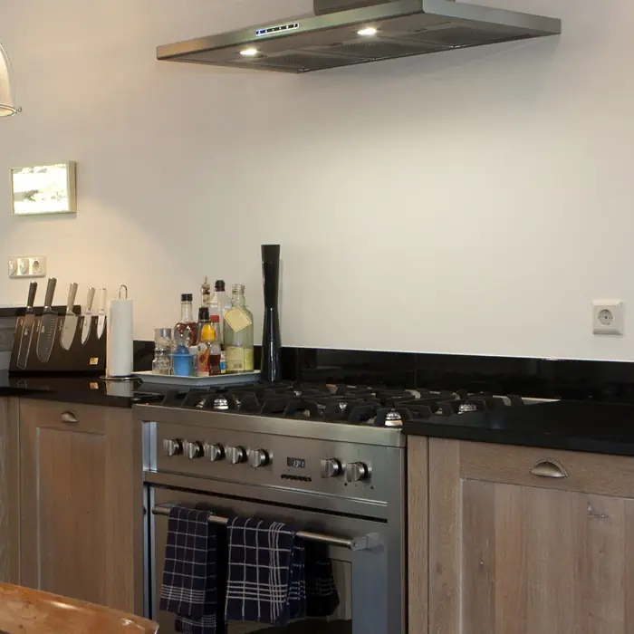 Keuken in licht eiken met een donker werkblad, een roestvrijstalen fornuis en een afzuigkap.