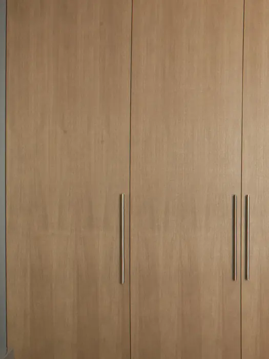 Detail van een kastenwand in licht eiken met hoge deuren en slanke verticale grepen.