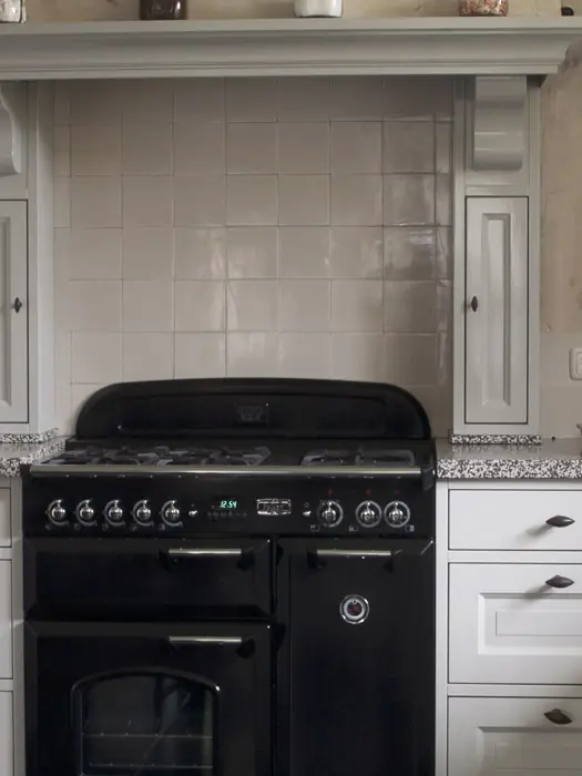 Klassieke keuken in gebroken wit met een schouw boven het fornuis, een wandklok en een stenen werkblad.