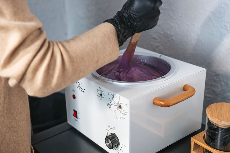 Warme wax wordt uit een verwarmingsapparaat geschept.