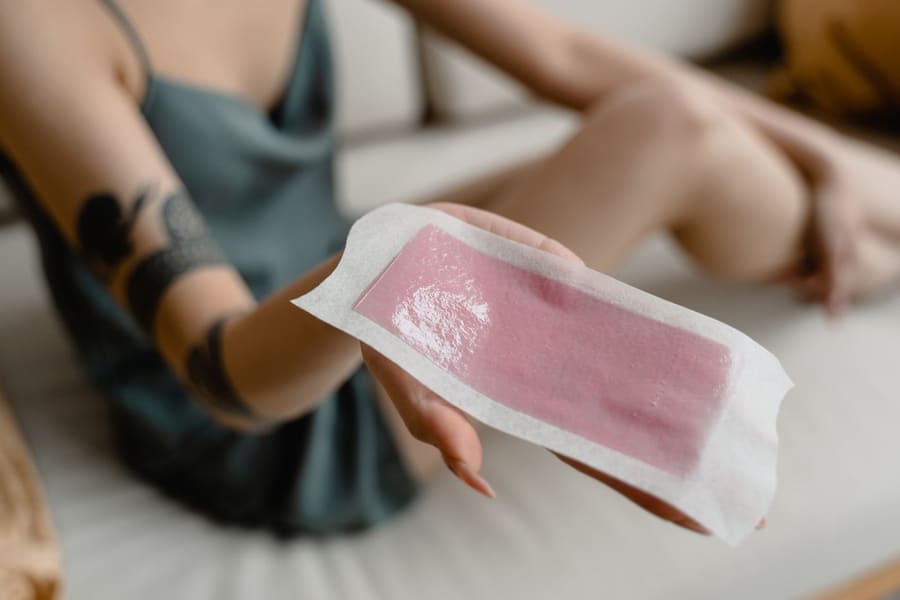 Een hand houdt een gebruikte waxstrip vast.