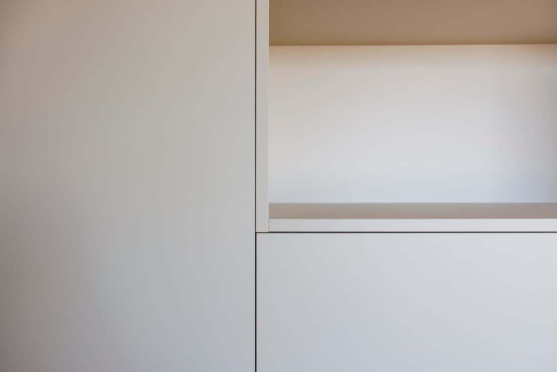 Detail van een strakke witte kastwand met open vak