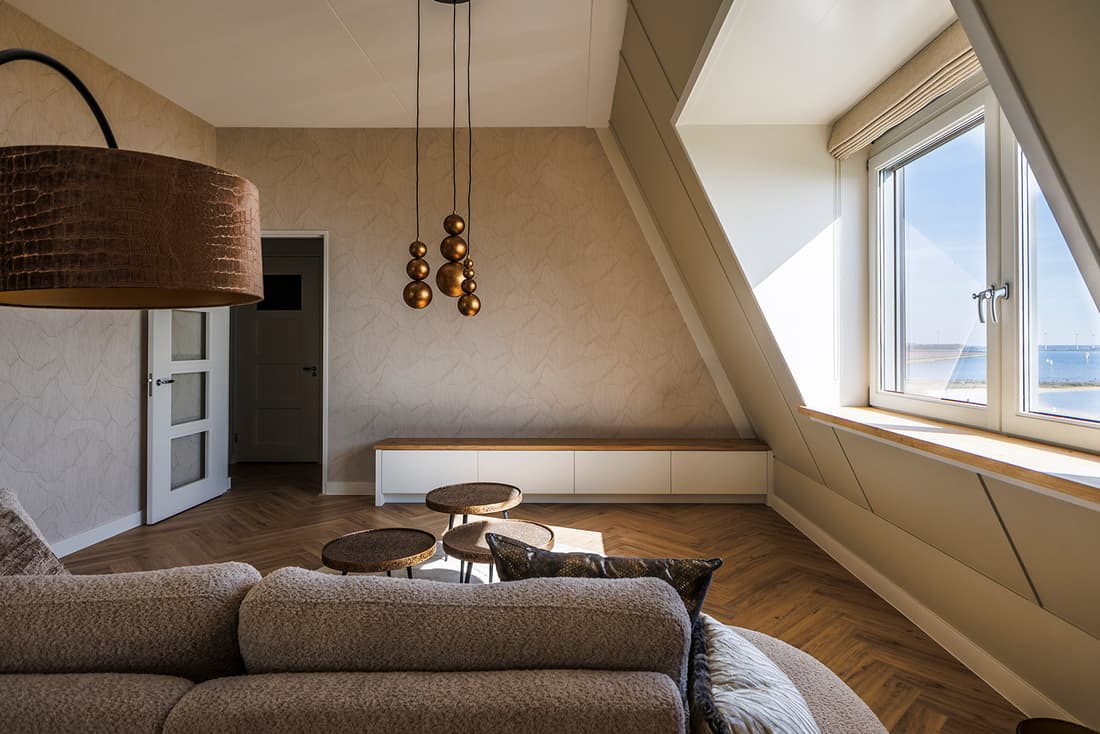 Woonkamer onder een schuin dak met maatwerk kast en bronzen hanglampen