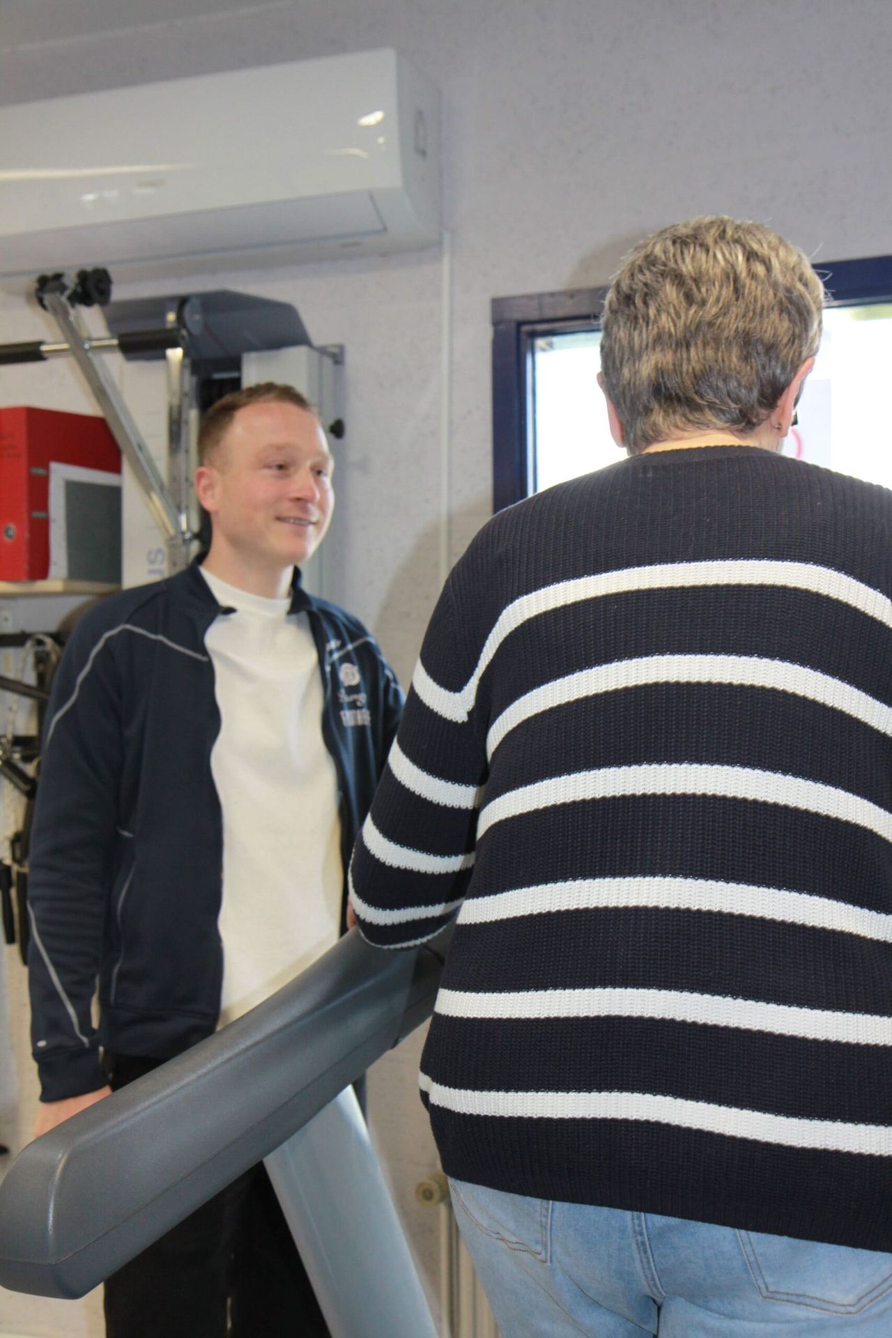 Fysiotherapeut begeleidt een oudere patiënt bij een trainingstoestel