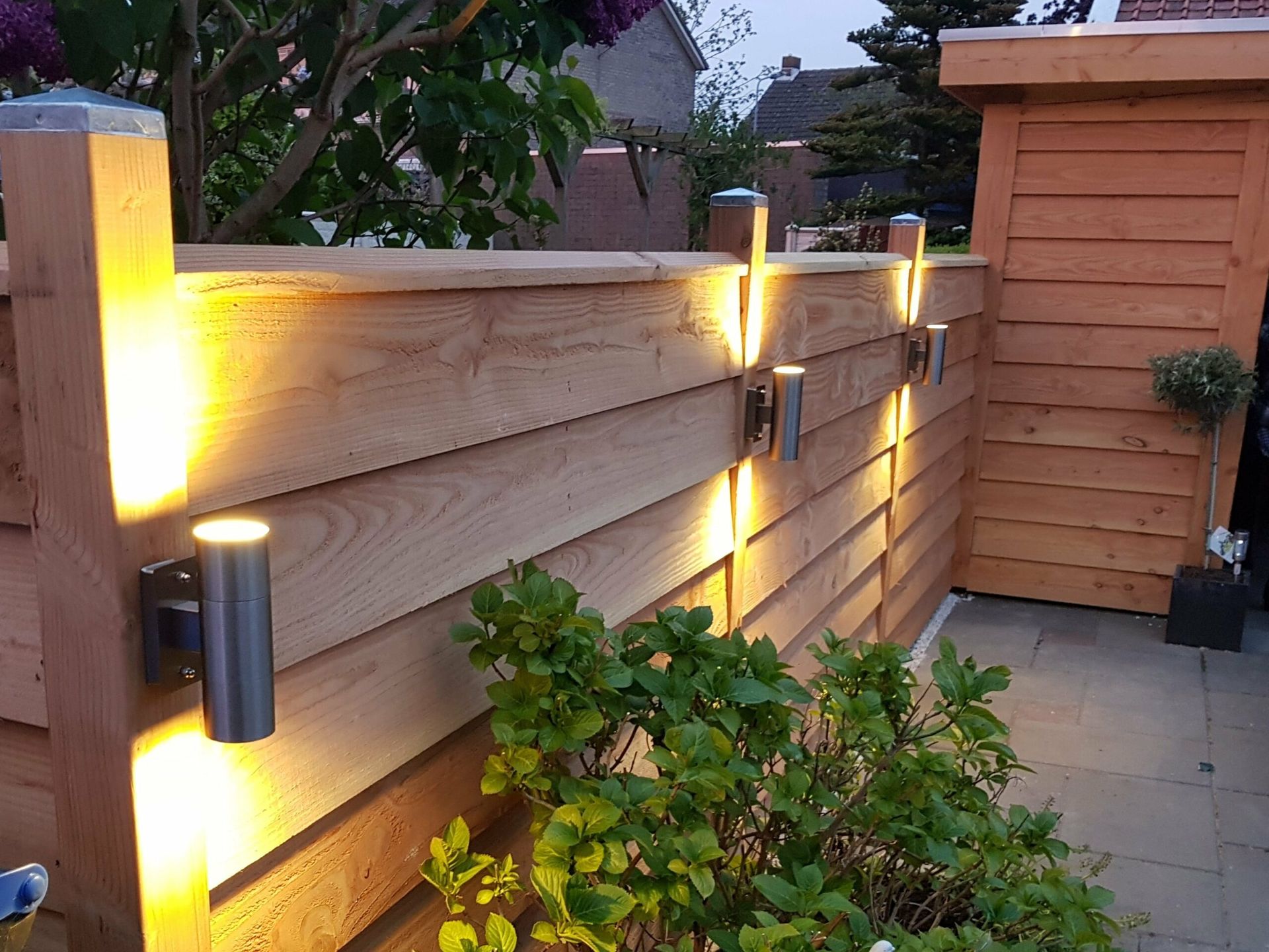 Zelfgebouwde houten tuinschutting met sfeerverlichting, gerealiseerd door J & J Timmerwerken