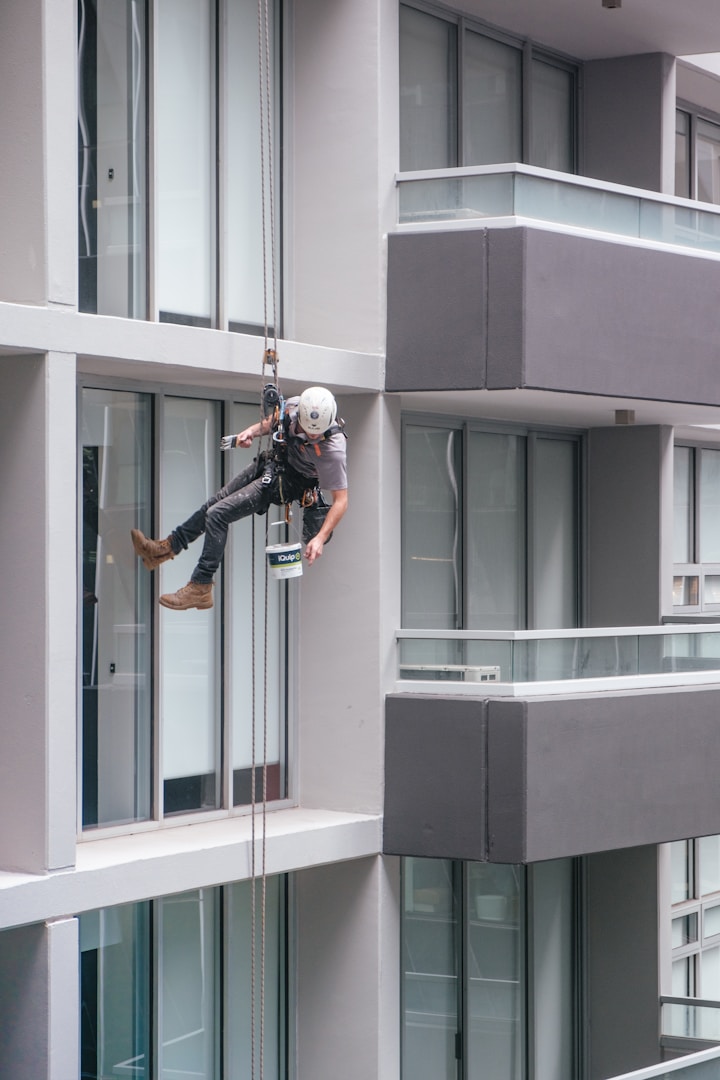 Schilder werkt hangend aan touwen op hoogte aan de gevel van een appartementengebouw