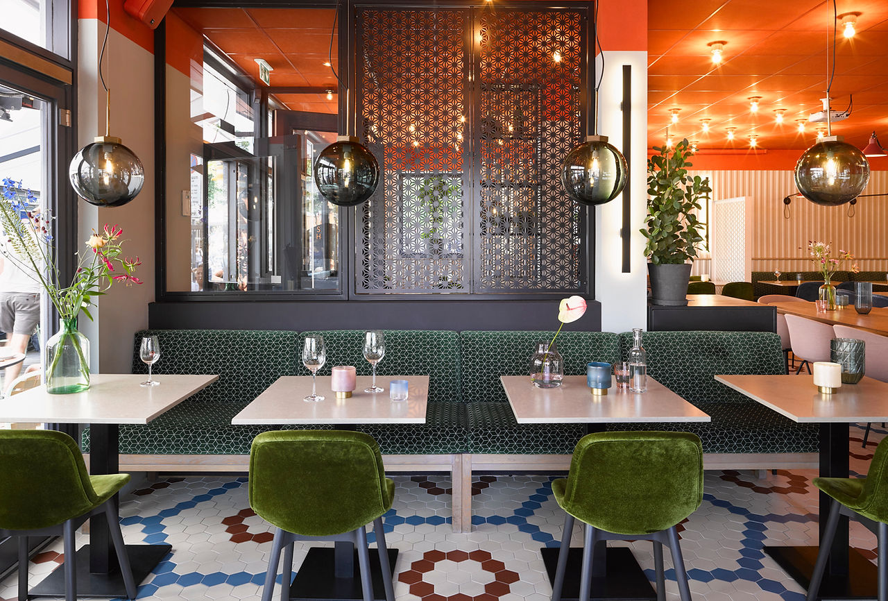 Groene fluwelen stoelen en een lange bank langs het raam, met de hexagonale tegelvloer