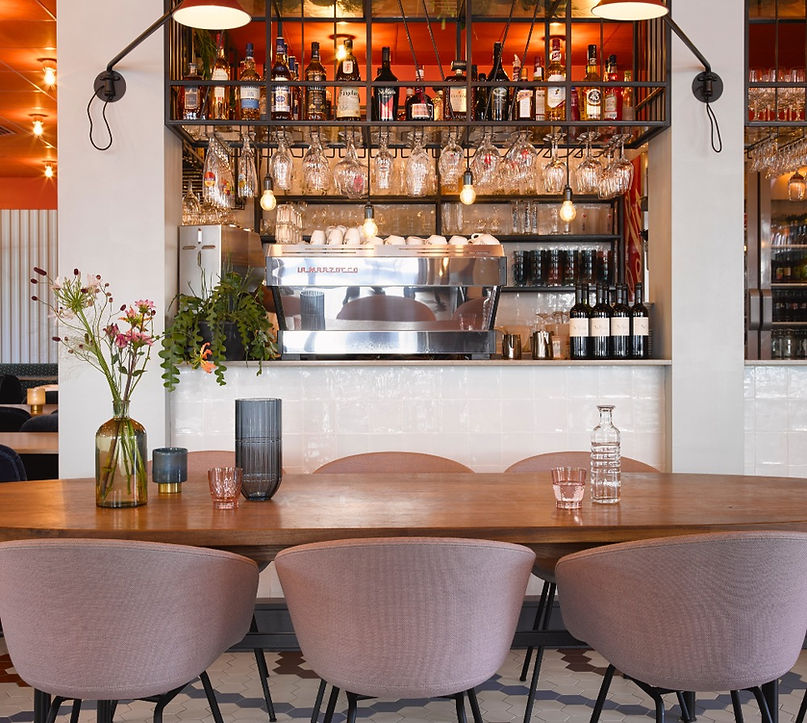 De grote houten tafel met roze stoelen en verse bloemen, met zicht op de zaal